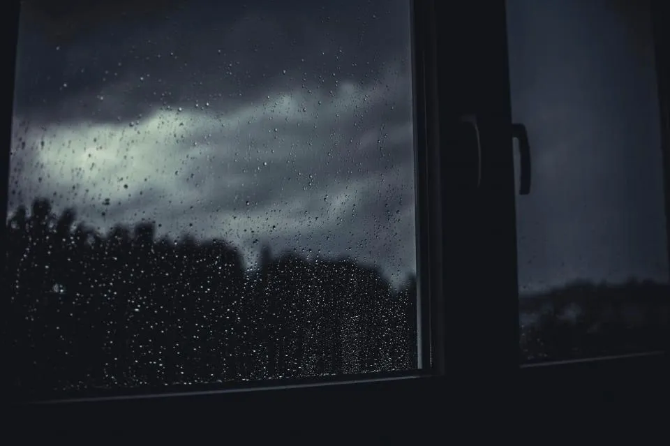 Rain running down a window at dusk, looking out at a dark sky over rooftops