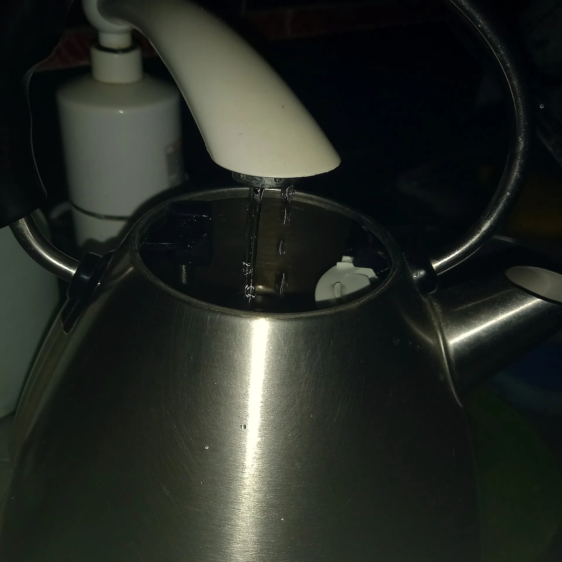 A stainless steel kettle being filled from a running kitchen tap